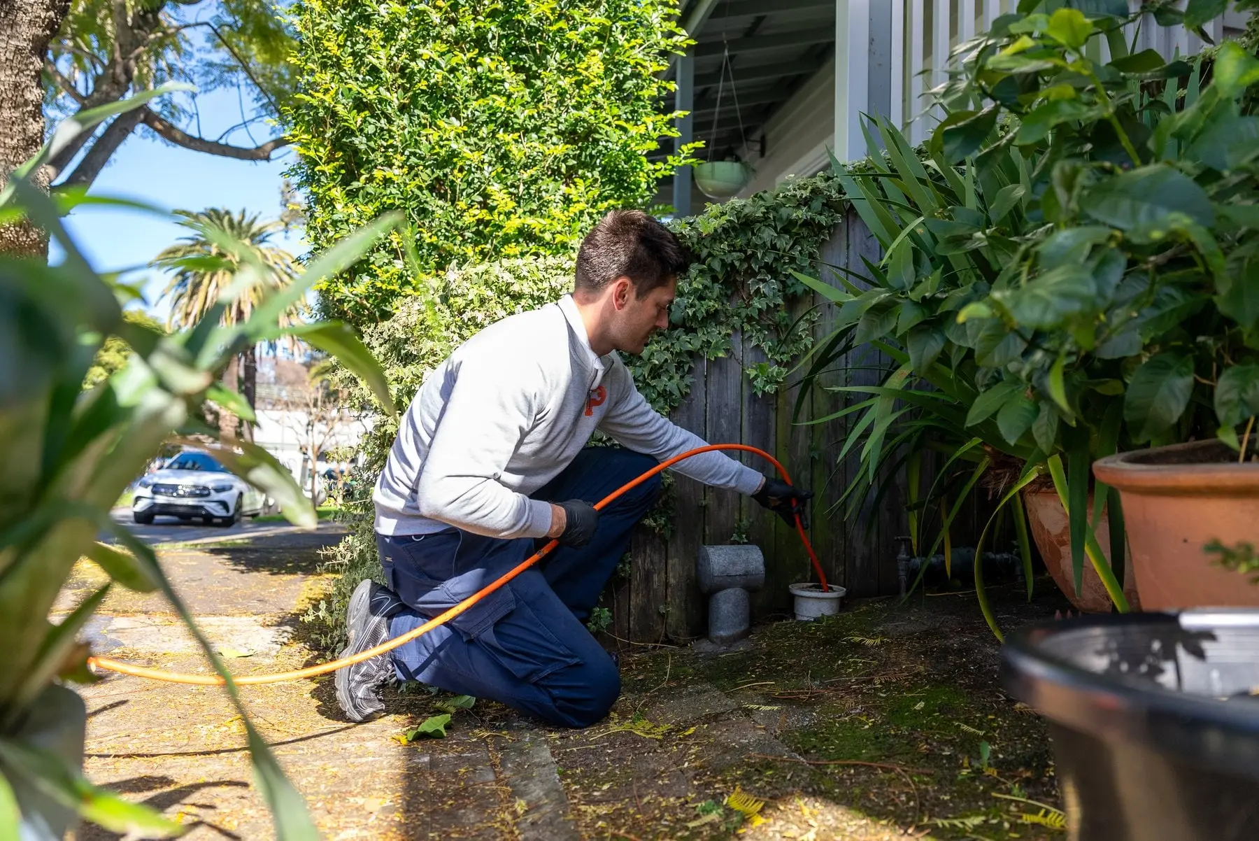 Plumber feeding a drain cleaning cable into an outdoor inspection opening