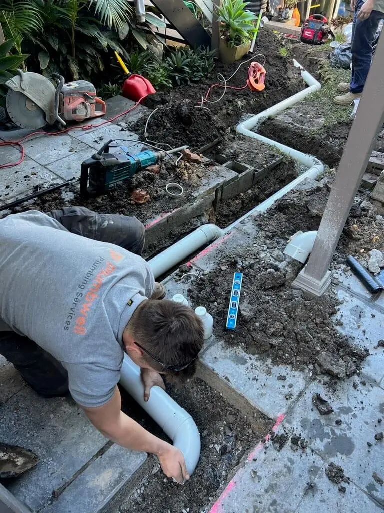 Plumber kneeling to join a new stormwater pipe in a trench