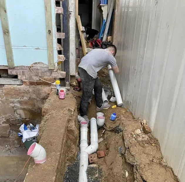 Plumber laying new drainage pipe in a trench beside a house