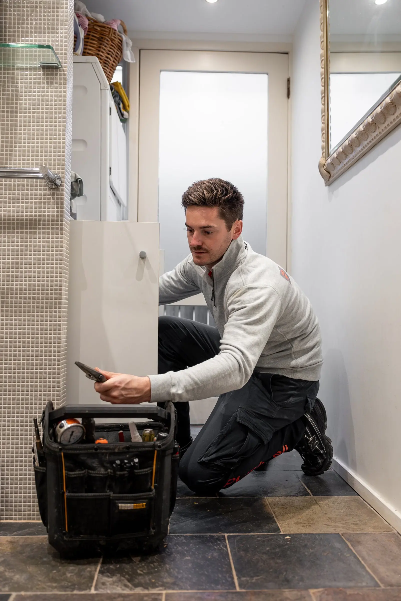 Plumber kneeling beside his tool bag in a bathroom