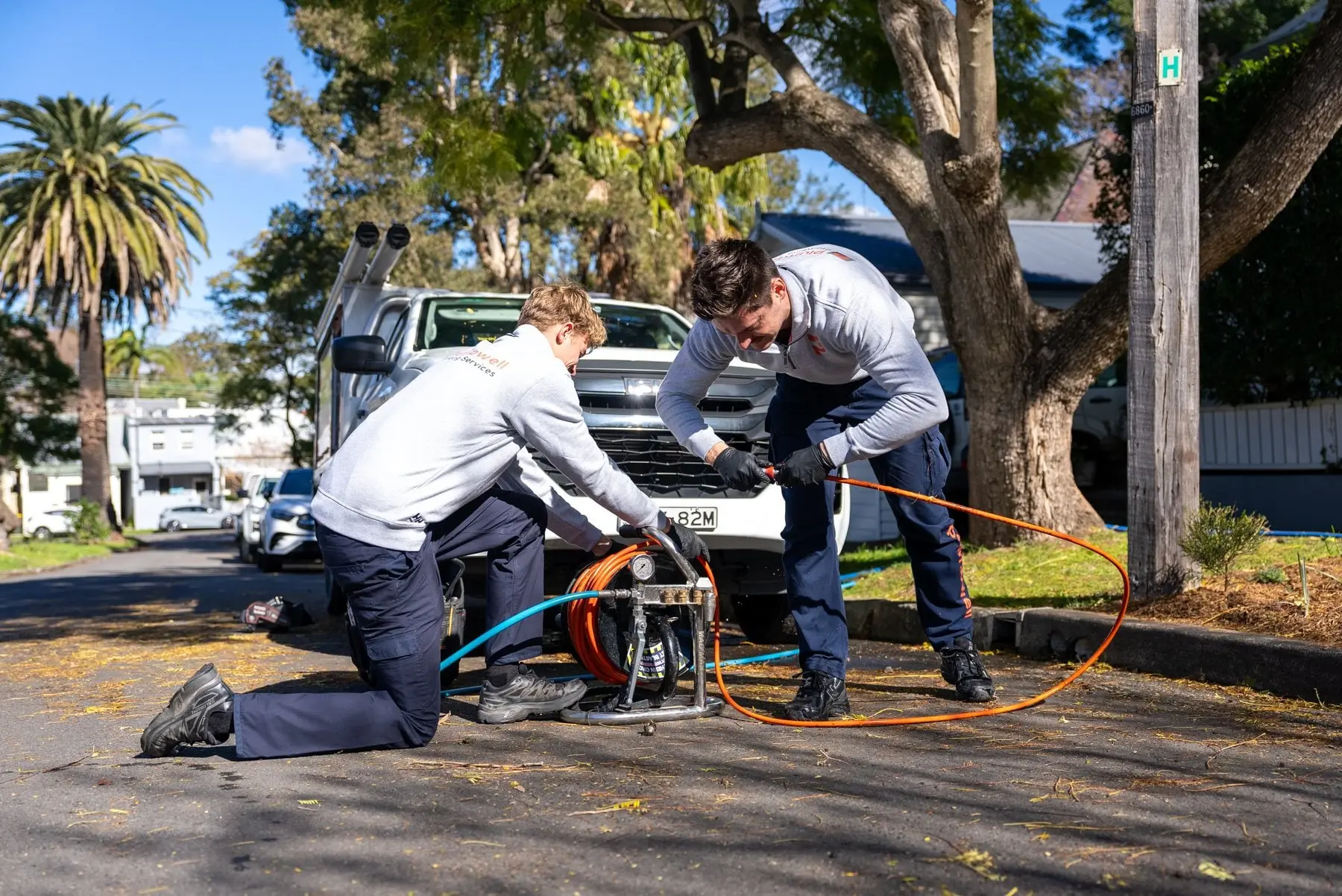 Two plumbers feeding a drain cable into a sewer line at the kerb