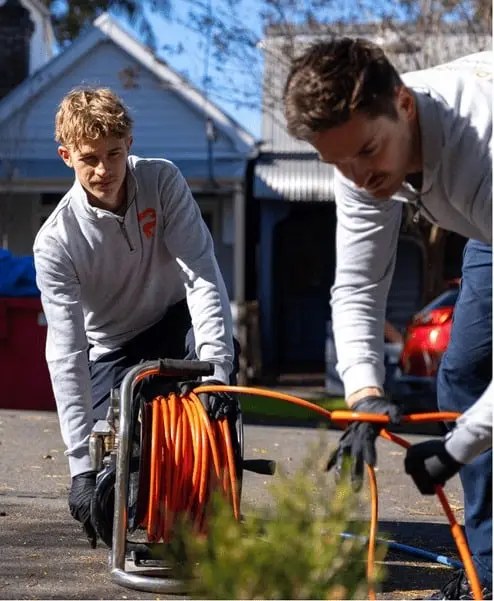 Two plumbers unwinding a drain jetting hose reel in a driveway