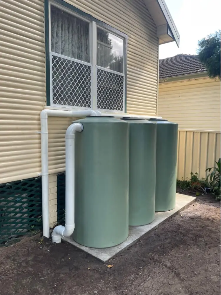 Three rainwater tanks connected to downpipes beside a weatherboard house