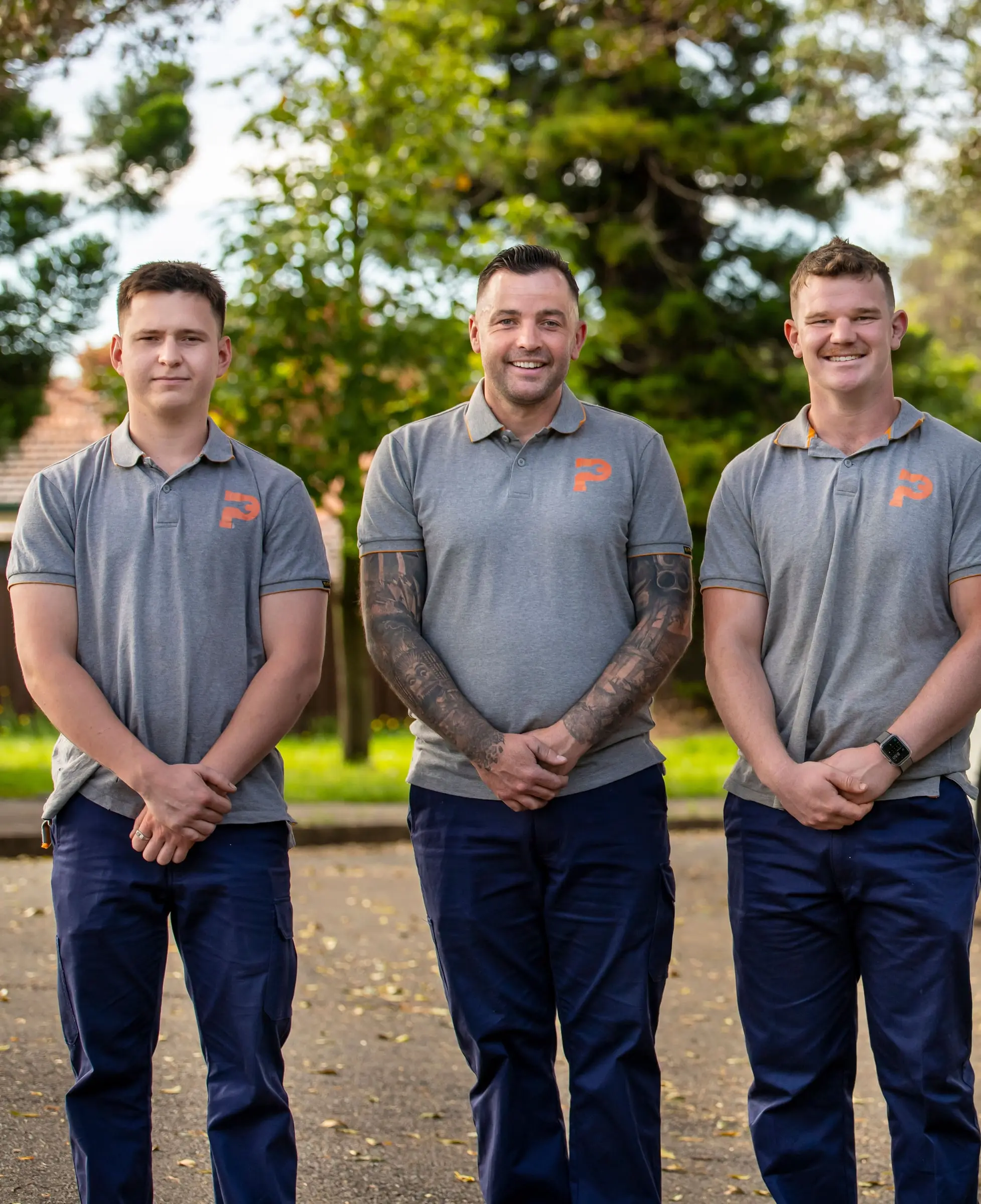 Three smiling plumbers in branded polo shirts standing on a suburban street
